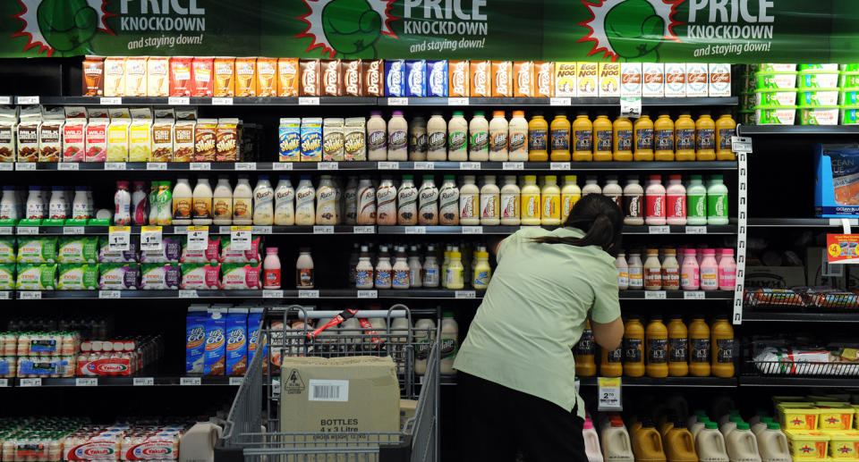 A Woolworths employee stocking a milk fridge in store. 