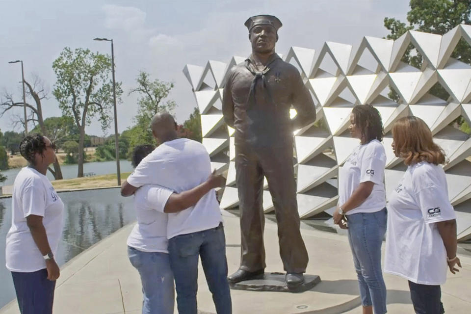 This image released by National Geographic shows family members surrounding a memorial honoring mess attendant Doris Miller in Waco, Texas. Miller, who shot down enemy planes during the attack on Pearl Harbor, is featured in the series "Erased: WW2's Heroes of Color." (National Geographic via AP)