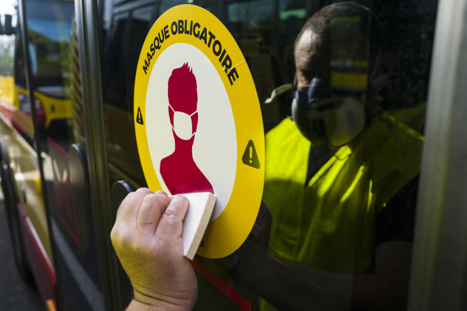 A man places a sticker reading 'Mandatory Masks' on a School bus door in Mulhouse, eastern France, on May 8, 2020, as France readies for May 11, easing of the lockdown which began on March 17, to stop the spread of the Covid-19 pandemic caused by the novel coronavirus. - France is scheduled May 11, to start easing a lockdown that began in mid-March as the number of cases, hospitalisations and deaths show signs of slowing. (Photo by SEBASTIEN BOZON / AFP) (Photo by SEBASTIEN BOZON/AFP via Getty Images)