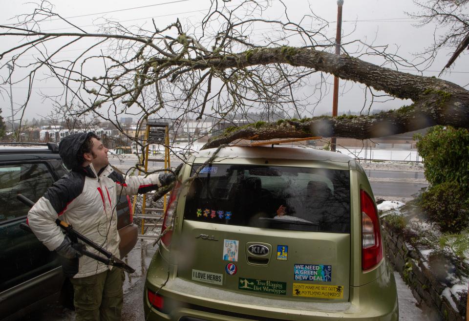 Kai Burley works to lighten the load of a tree limb from the top of his mother’s car as the Willamette Valley digs out from under an ice storm that paralyzed parts of Oregon for days.