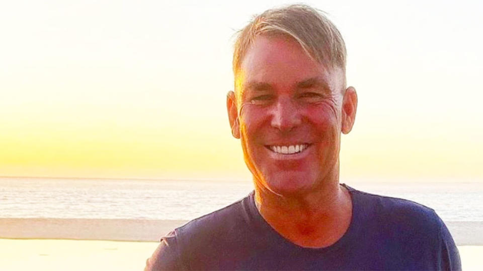 Shane Warne is posing for a photo here in front of a beach at sunset.