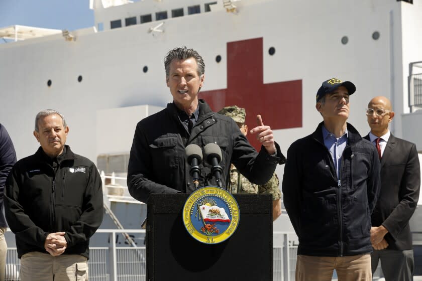 LOS ANGELES, CALIFORNIA-MARCH 27, 2020-California Governor Gavin Newsom speaks in front of the hospital ship USNS Mercy that arrived into the Port of Los Angeles on Friday, March 27, 2020, to provide relief for Southland hospitals overwhelmed by the coronavirus pandemic. Also attending the press conference were Director Mark Ghilarducci, Cal OES, left, Los Angeles Mayor Eric Garcetti, second from right, and Dr. Mark Ghaly, Secretary of Health and Human Services, far right, along with others not shown. (POOL PHOTOGRAPHS by Carolyn Cole/Los Angeles Times)