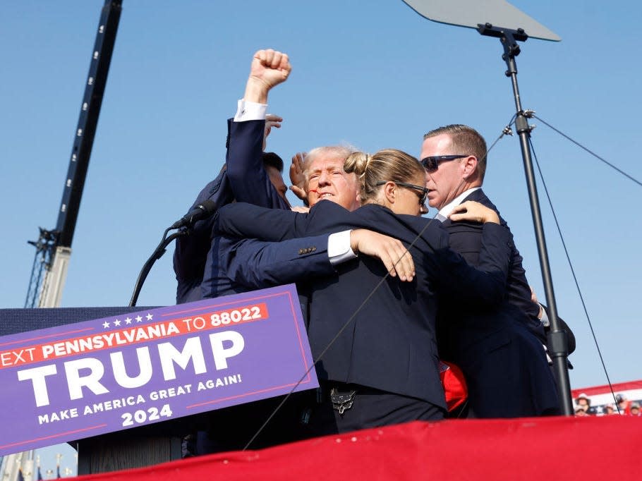 Donald Trump is rushed offstage after a shooting at a campaign rally. Secret Service members surround him as he raises his fist in the air.