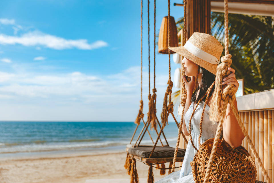 Travel summer vacation concept, Happy traveler asian woman with hat and dress relax on swing in beach cafe, Koh Chang, Thailand