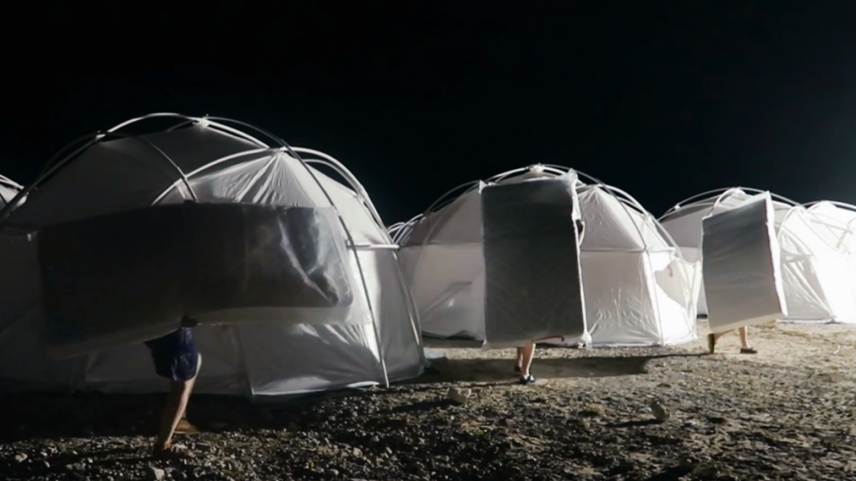 An image of large, white, dome-shaped tents on a beach at night.