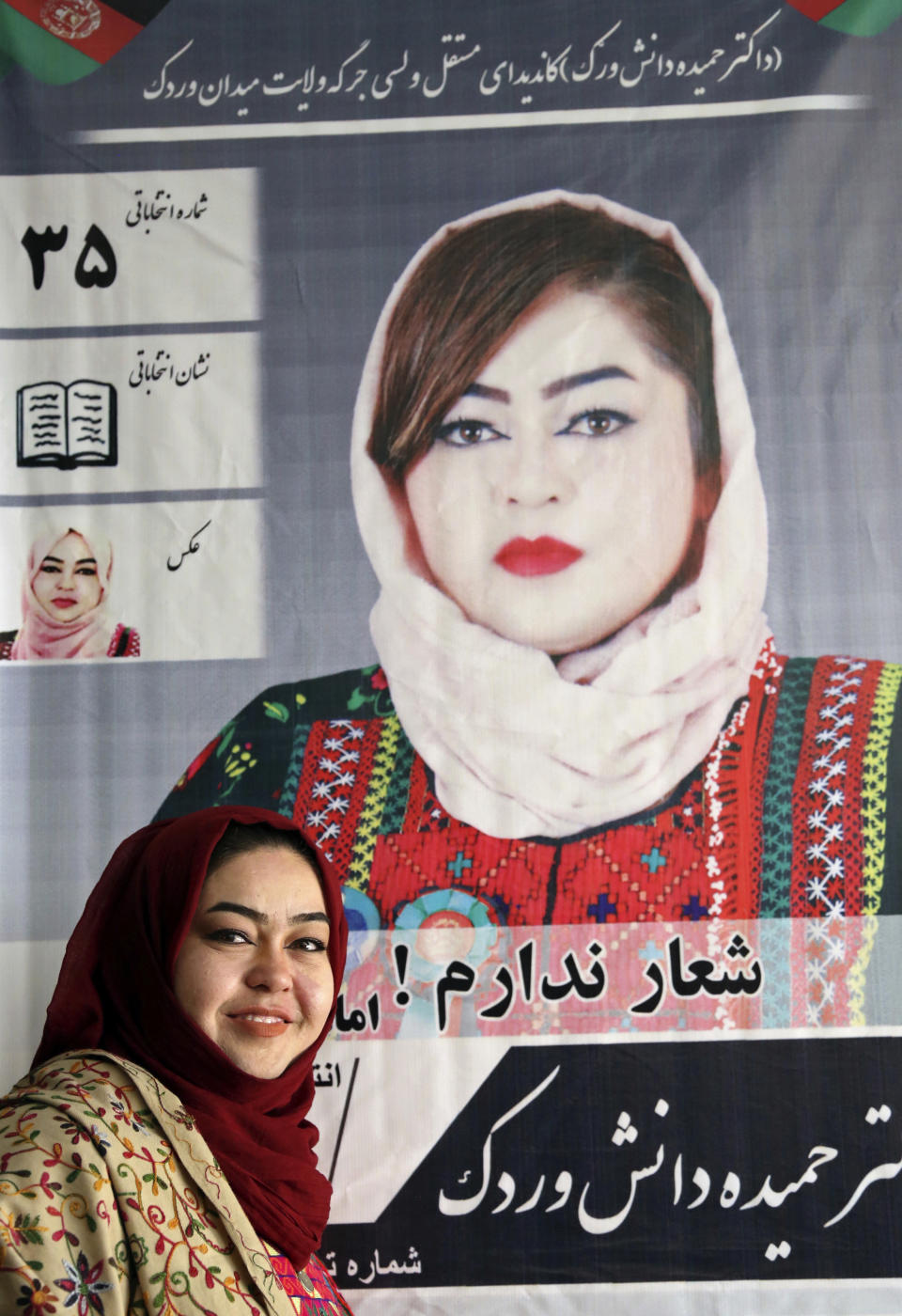 In this Sunday, Oct. 14, 2018 photo, Hameeda Danesh, a candidate for Parliament, hoping to represent the deeply conservative district of Jalrez in central Wardak province, poses for photograph with an elections poster, at her office in Wardak, Afghanistan. Danesh says the elections Saturday are key to countering the conservatism that stifles education, other opportunities for women. (AP Photo/Rahmat Gul)