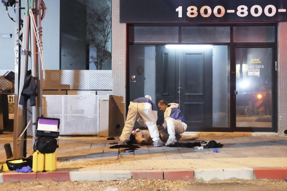 Israeli police examine a body at the scene of shooting attack In Hadera, Israel, Sunday, March 27, 2022. A pair of gunmen killed two people and wounded four others in a shooting spree in central Israel before they were killed by police, according to police and medical officials. The identity of the gunmen was not immediately known, but police called them "terrorists," the term usually used for Arab assailants. (AP Photo/Ariel Schalit)