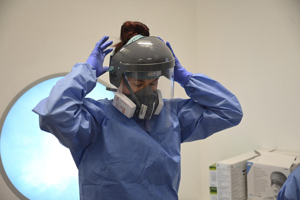 A member of the clinical staff puts on Personal Protective Equipment PPE in the intensive care unit at the Royal Papworth Hospital in Cambridge, England, Tuesday May 5, 2020. (Neil Hall/Pool via AP)