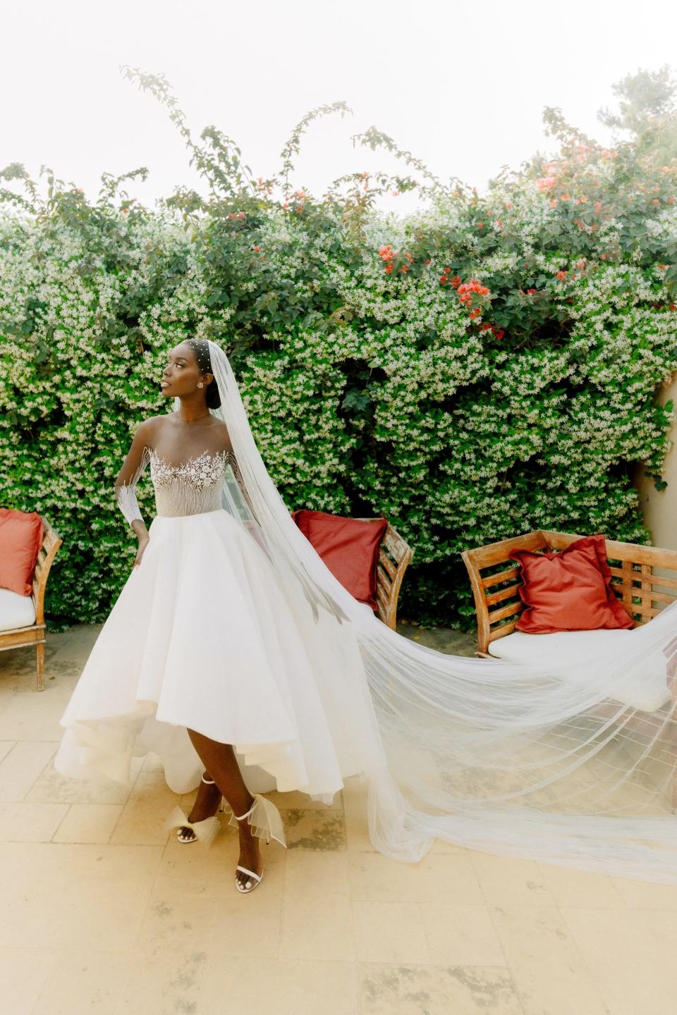 A bride stands in her wedding dress in front of a wall of greenery.