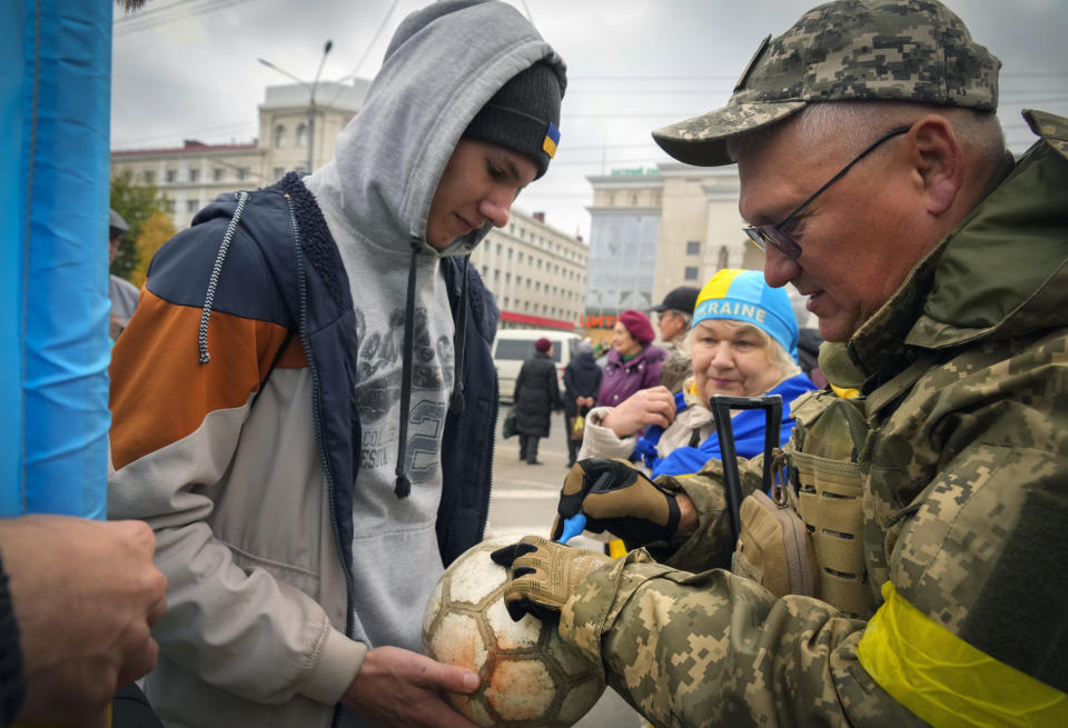 A Ukrainian soldier writes: "From the Ukrainian Armed Forces" on the soccer ball of a local resident in central Kherson, Ukraine, Sunday, Nov. 13, 2022. The Russian retreat from Kherson marked a triumphant milestone in Ukraine's pushback against Moscow's invasion almost nine months ago. (AP Photo/Efrem Lukatsky)