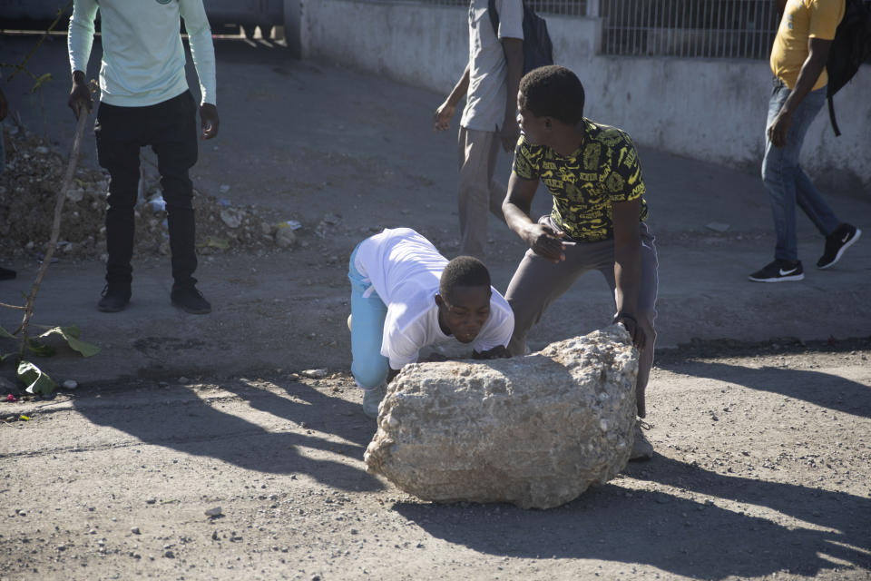Protesters try to move a chunk of concrete to block a street during a protest by factory workers demanding salary increases in Port-au-Prince, Haiti, Wednesday, Feb. 23, 2022. It is the first day of a three-day strike organized by factory workers who also shut down an industrial park earlier this month to protest pay. (AP Photo/Odelyn Joseph)