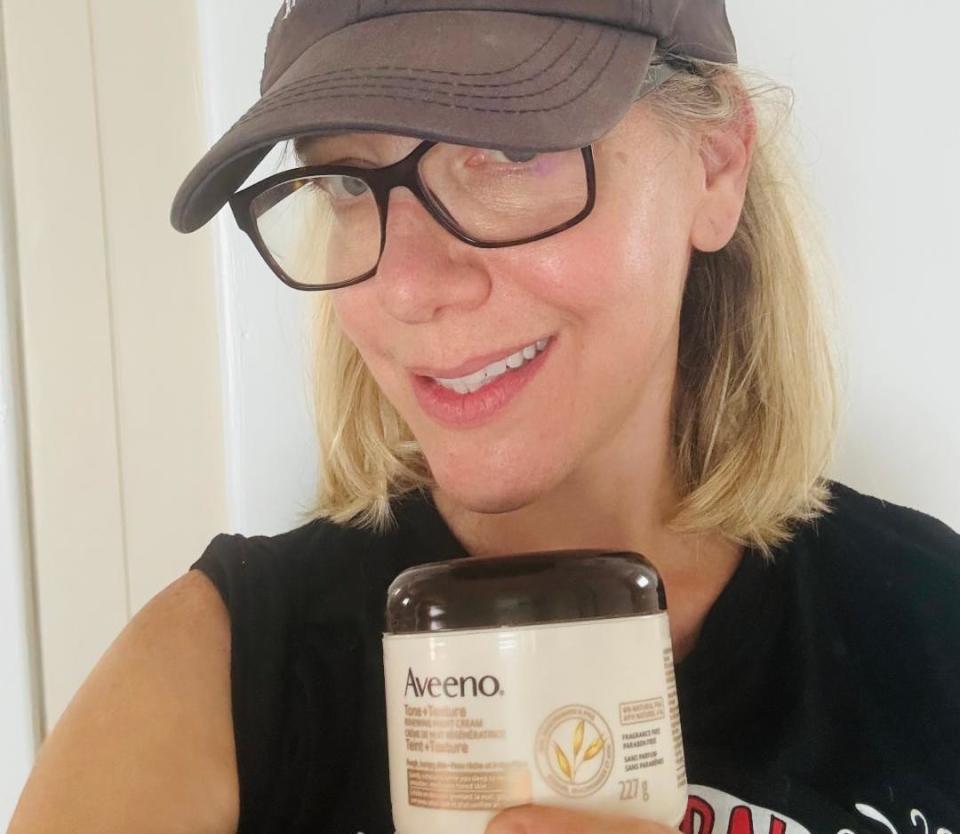 blonde woman wearing hat holding aveeno skin cream