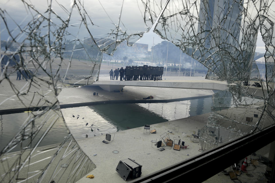 Police stand on the other side of a window at Planalto Palace that was shattered by protesters, supporters of Brazil's former President Jair Bolsonaro, after they stormed the official workplace of the president in Brasilia, Brazil, Sunday, Jan. 8, 2023. (AP Photo/Eraldo Peres)