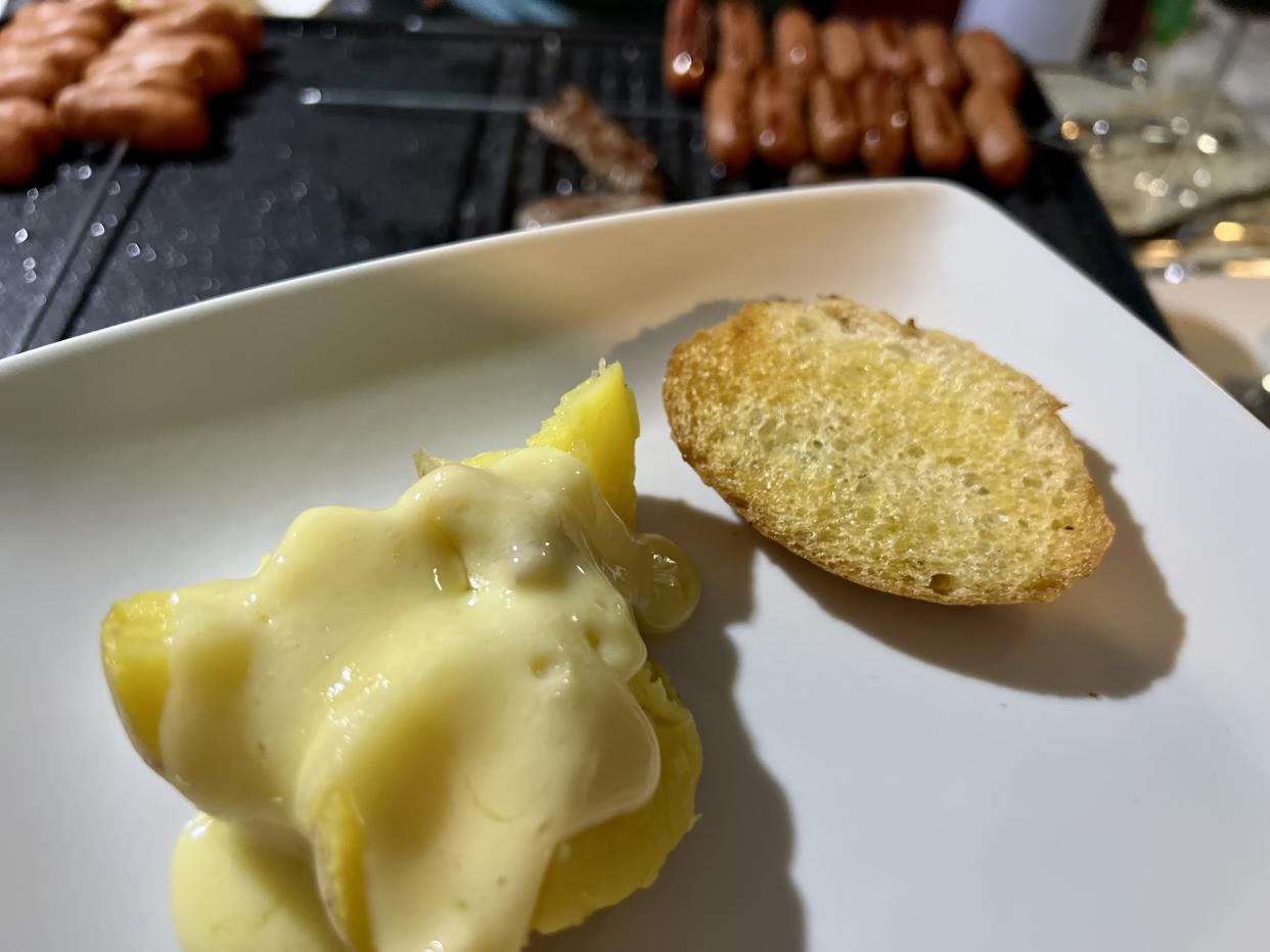 Melted raclette atop boiled potatoes, with a slice of baguette heated on the grill. (Photo: Terri Peters)