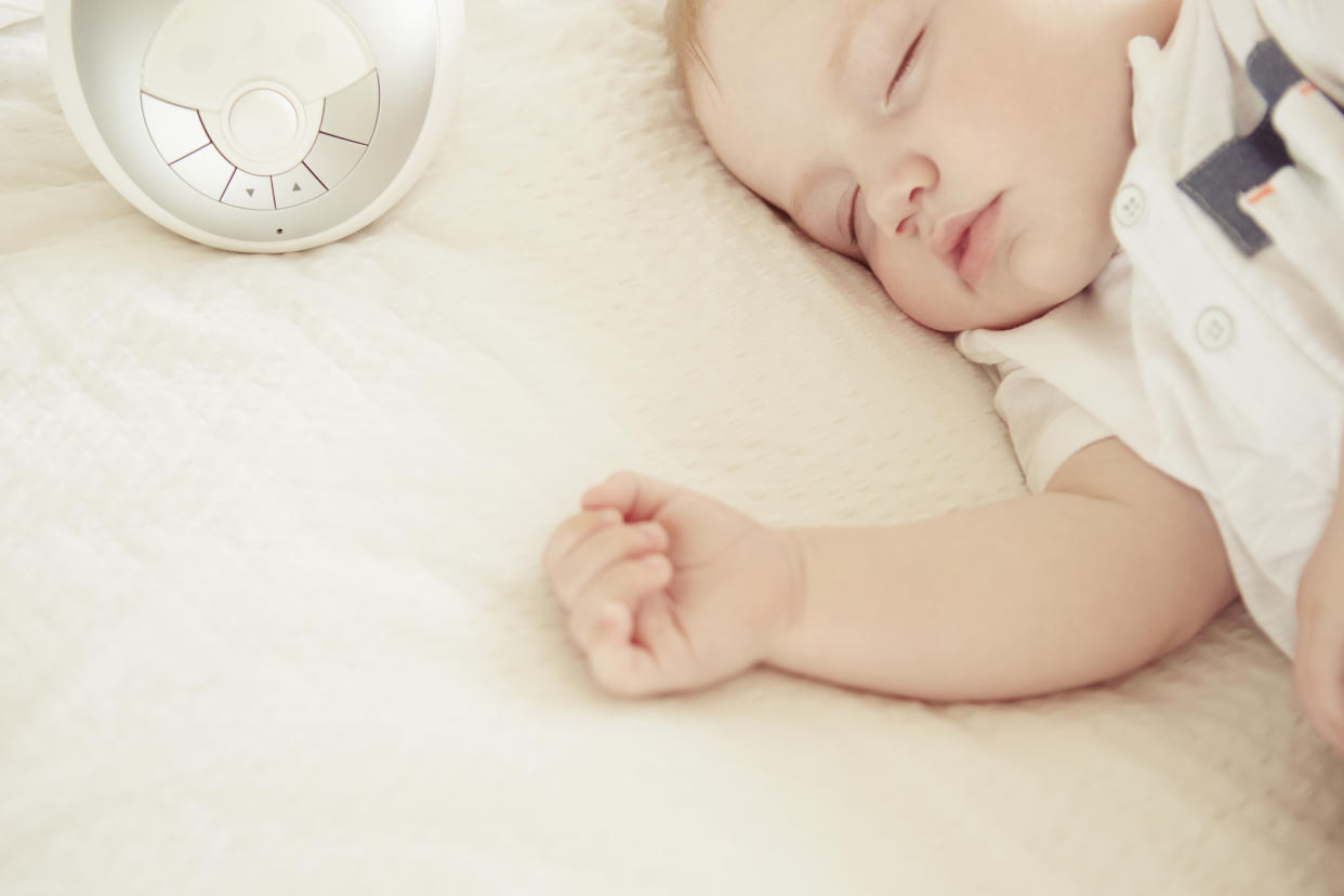 A baby is sleeping on a bed next to a white noise machine.