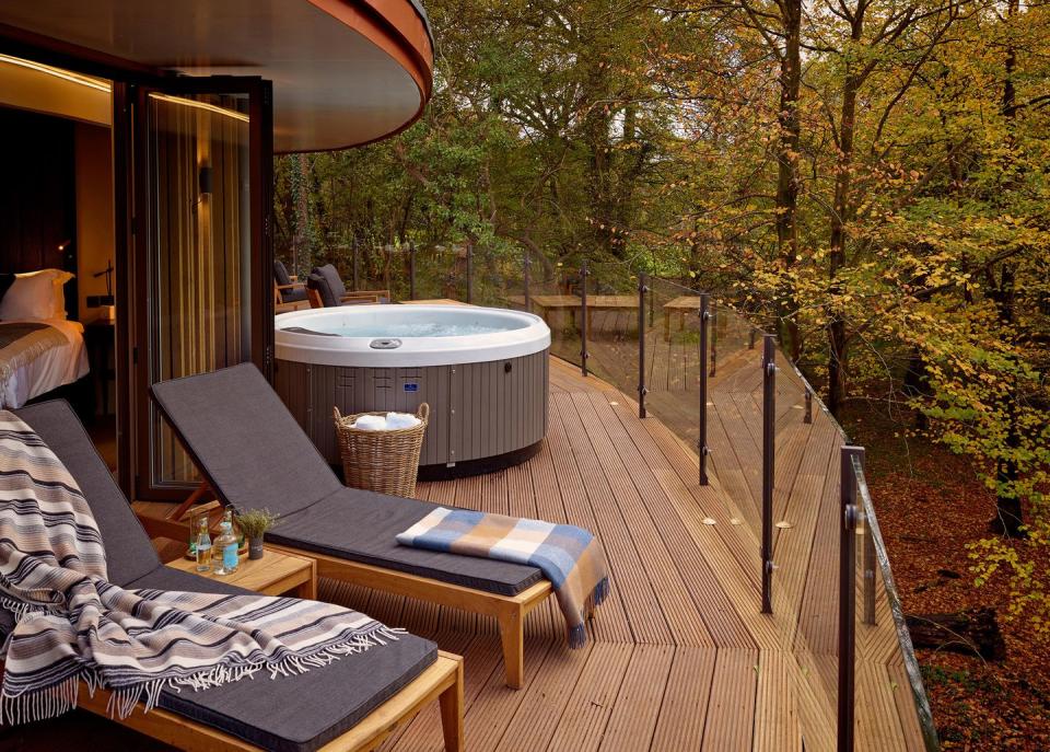 chewton glen treehouse deck with hot tub and a table with a chair and a table