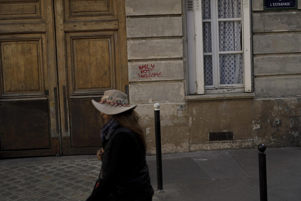 A woman walks past a graffiti reading "Emily Not Welcome" scrawled on part of the facade of the building where the fictional character Emily Cooper lives, at 1 Place de d'Estrapade, in Paris, Wednesday, April 19, 2023. The immense success of the Netflix series "Emily in Paris" has transformed a quiet, untouched square in the French capital into a tourist magnet. (AP Photo/Thibault Camus)