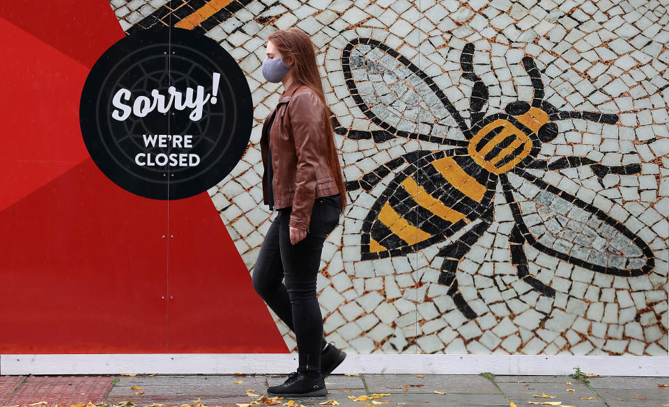 A person wearing a face mask walks past a poster of the Manchester Bee in Albert Square, Manchester as the Government is preparing to impose stringent new coronavirus controls on 2.8 million people after talks with the local leaders for Greater Manchester failed to reach agreement. Leaders have been given until midday on Tuesday to reach a deal, or face unilateral Government action, after 10 days of negotiations failed to reach an agreement.