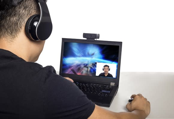 A man wearing a headset and looking at a laptop screen