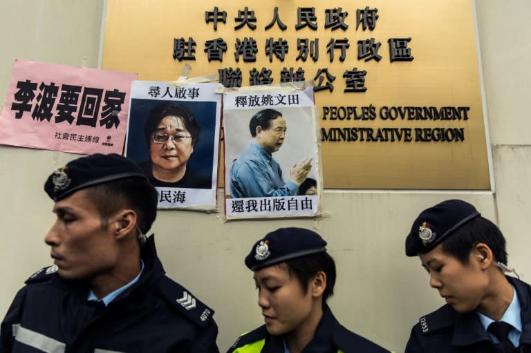 Police walk past missing person notices of Gui Minhai (L), one of five missing booksellers from the Mighty Current publishing house and Yau Wentian (R), a Hong Kong publisher jailed for 10 years over a book critical of Chinese President Xi Jinping