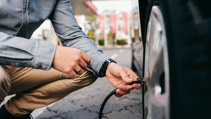 Close up of man crouching on the gas station and inflating tire.