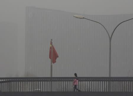 A woman wearing a protective mask walks past a Chinese national flag on a pedestrian overpass on a heavily polluted day in Beijing, December 25, 2015. REUTERS/Kim Kyung-Hoon