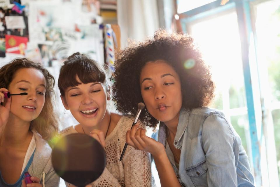 Group of three people applying cosmetic supplies in front of mirror.