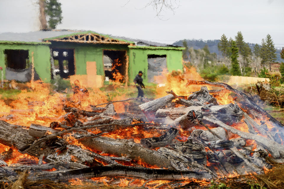 A worker monitors a burn pile while clearing vegetation, Wednesday, Oct. 25, 2023, in Paradise, Calif. His crew was clearing the property of dead wood and flammable vegetation to meet defensible space requirements Paradise adopted following the Camp Fire. (AP Photo/Noah Berger)