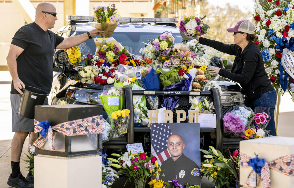 Retired Orange police officer Rob Thorsen, left, and his wife Kappy, of Yorba Linda, place flowers on a memorial for Huntington Beach police officer Nicholas Vella outside the Huntington Beach Police Department in Huntington Beach, Sunday, Feb. 20, 2022. Officer Vella, 44, a 14-year veteran of the Huntington Beach Police Department was killed in a helicopter crash Saturday in Newport Beach. (Leonard Ortiz/The Orange County Register via AP)