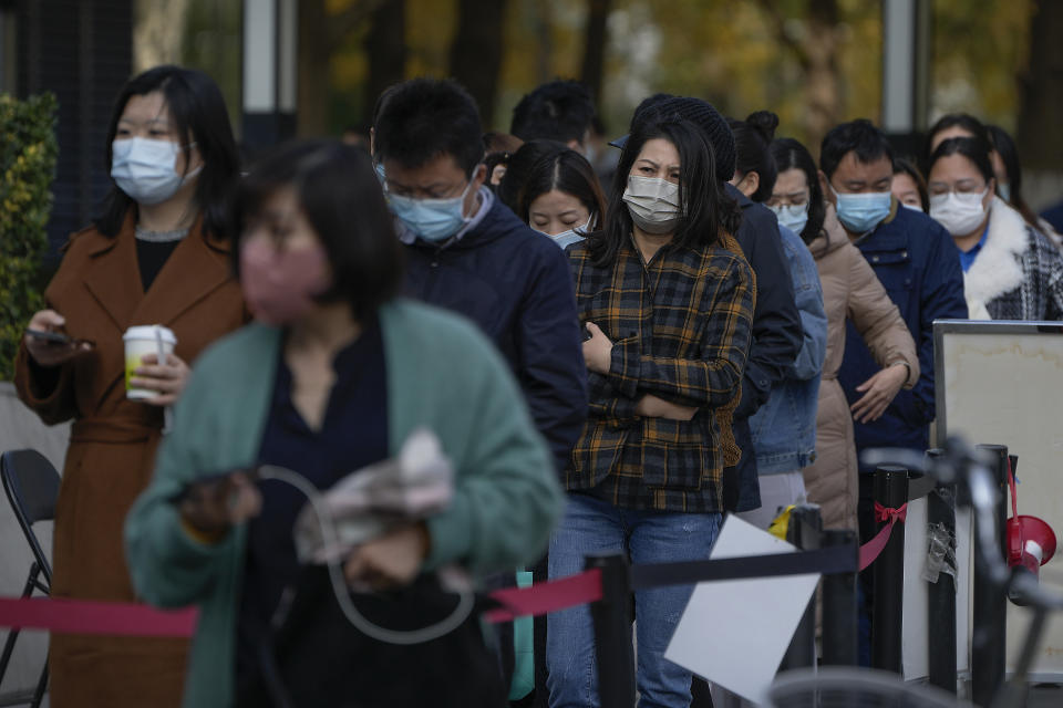 People wearing face masks line up for their routine COVID-19 throat swabs at a coronavirus testing site in Beijing, Tuesday, Nov. 1, 2022. Visitors to Shanghai Disneyland were temporarily blocked from leaving as part of virus testing that extended to more than 400,000 people, the city government announced Tuesday. (AP Photo/Andy Wong)