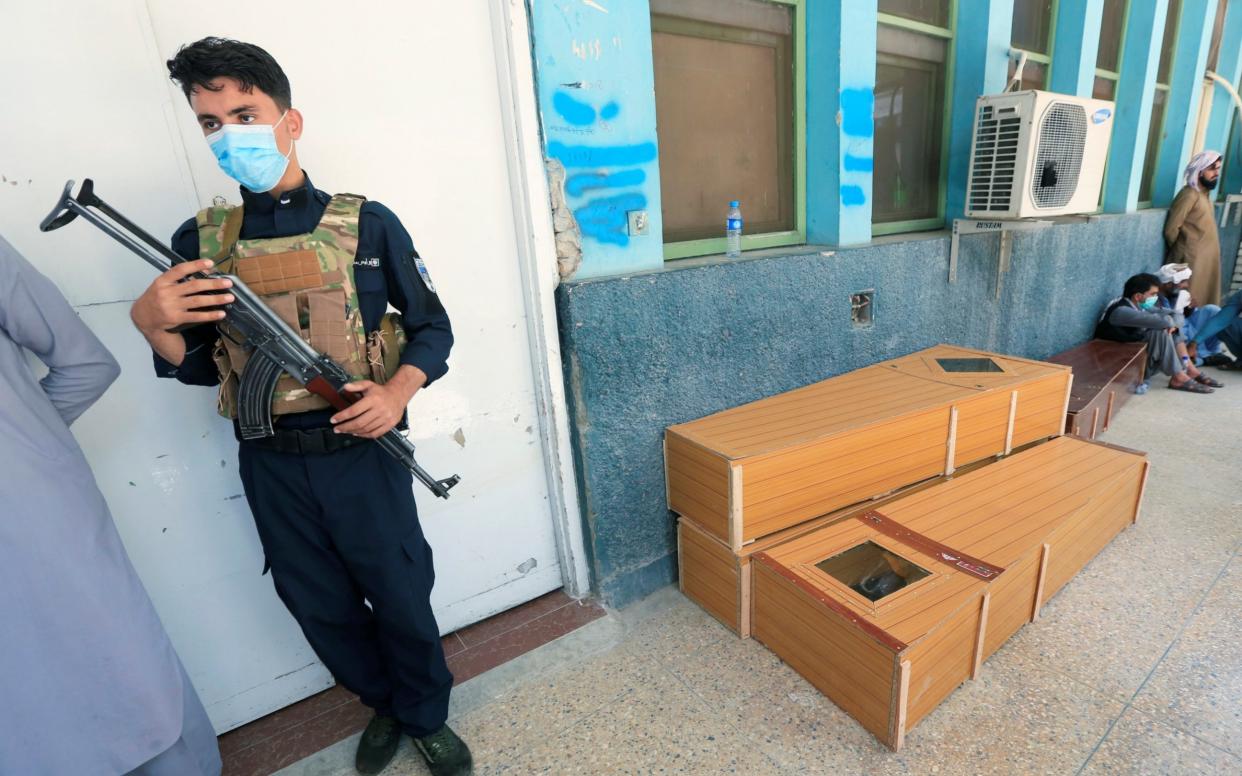 An Afghan policeman stands next to empty coffins which are prepared for polio vaccination health workers who were shot and killed by unknown gunmen at separate locations in Jalalabad - Reuters