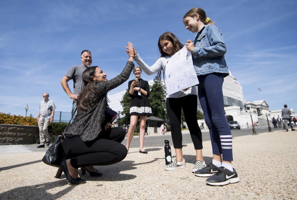 Rep. Alexandria Ocasio-Cortez, D-N.Y., high-fives climate striking students Evelyn Seek, center, and Pema Duncan, right, as they hold their climate strike sign in front of the Capitol on Friday, Sept. 20, 2019. | Bill Clark—CQ-Roll Call via Getty Images