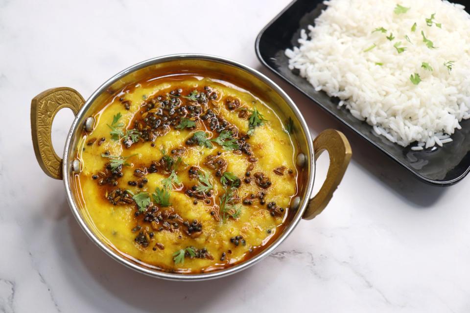 daal in a tin pot next to a plate of rice