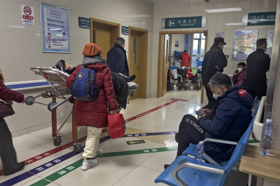 A man, right, browses his smartphone on a bench as an elderly patient is wheeled to an emergency hall in a hospital in Beijing, Saturday, Jan. 7, 2023. China has suspended or closed the social media accounts of more than 1,000 critics of the government's policies on the COVID-19 outbreak, as the country moves to further open up. (AP Photo/Andy Wong)