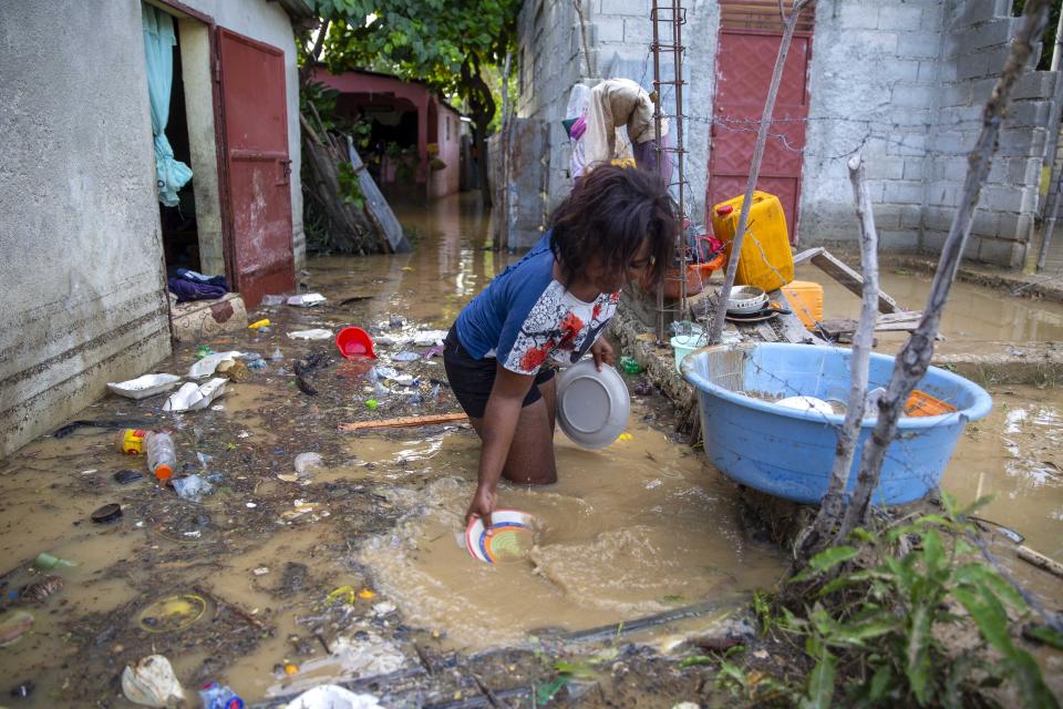 Yoleine Toussaint 22, removes mud from plates in front of her flooded house, one day after the passing of Tropical Storm Laura, in Port-au-Prince, Haiti, Monday, Aug. 24, 2020. Forecasters fear Laura could become a major hurricane along the U.S. Gulf Coast. (AP Photo/Dieu Nalio Chery)