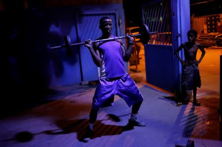 Wanderson Araujo lifts a loaded barbell as a child looks at him during his training session at a boxing school, in the Mare favela of Rio de Janeiro, Brazil, June 2, 2016. REUTERS/Nacho Doce