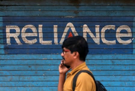 A man speaks on his mobile phone as he walks past a closed shop painted with an advertisement of Reliance Communications in Mumbai