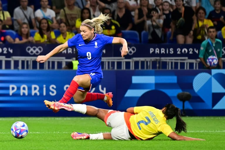 La delantera de Francia Eugenie Le Sommer (izquierda) salta por encima de la defensa de Colombia Manuela Vanegas durante el debut de ambas selecciones en el torneo de fútbol femenino de los Juegos Olímpicos de París 2024, en el Estadio de Lyon el 25 de julio de 2024. (Olivier CHASSIGNOLE)