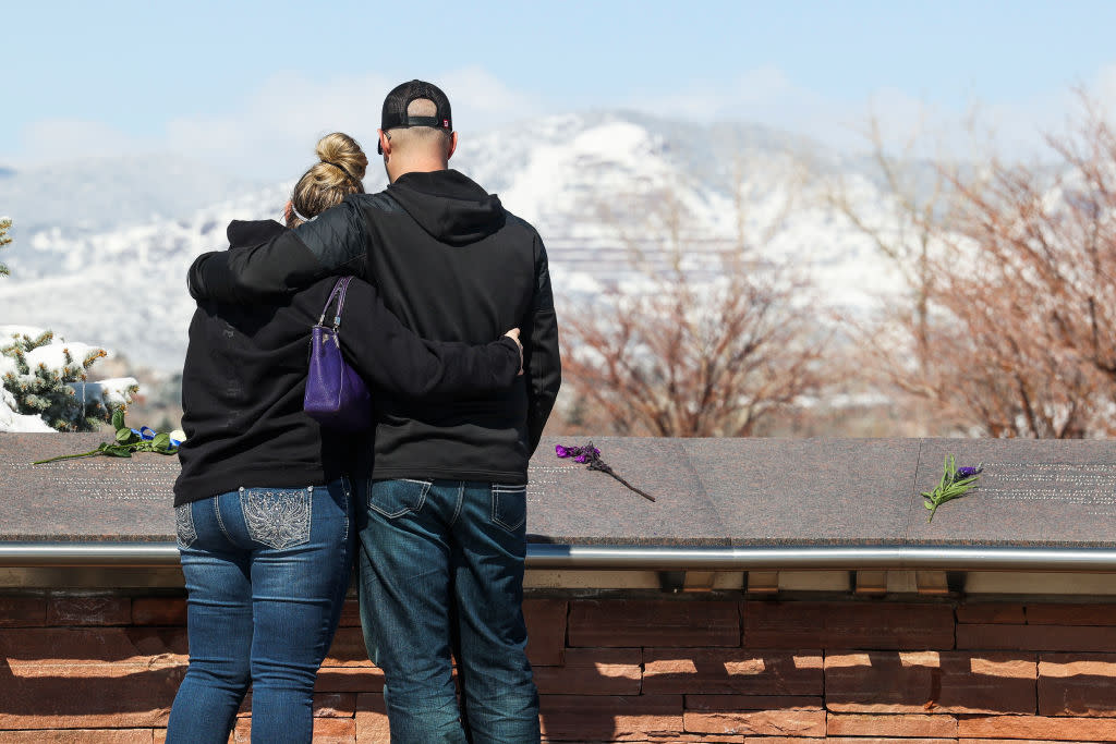 Two people embracing in front of a memorial with flowers.