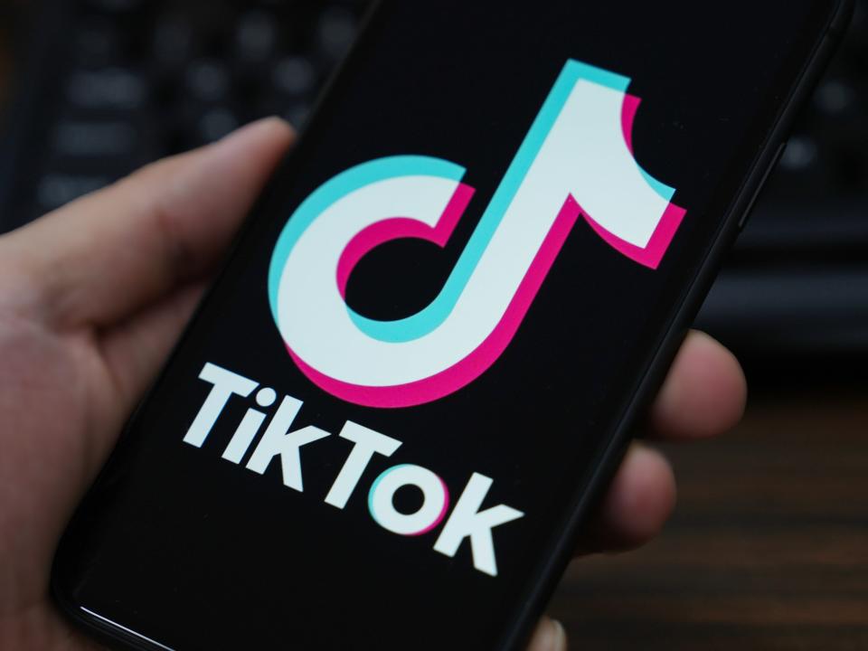 TikTok app logo shown on someone's phone being held in front of a keyboard.