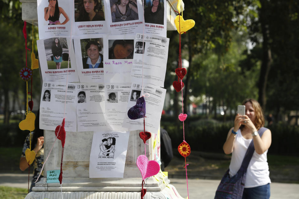 A woman takes a photo of a plinth covered with images of victims during a tribute for murdered women, in the Alameda park of Mexico City, Saturday, Aug. 24, 2019. A small group of women constructed a memorial made of hand-knit hearts. The knit-in on came on the heels of rowdy protests sparked by outrage over bungled investigations into alleged rapes of teenagers by local policemen. (AP Photo/Ginnette Riquelme)