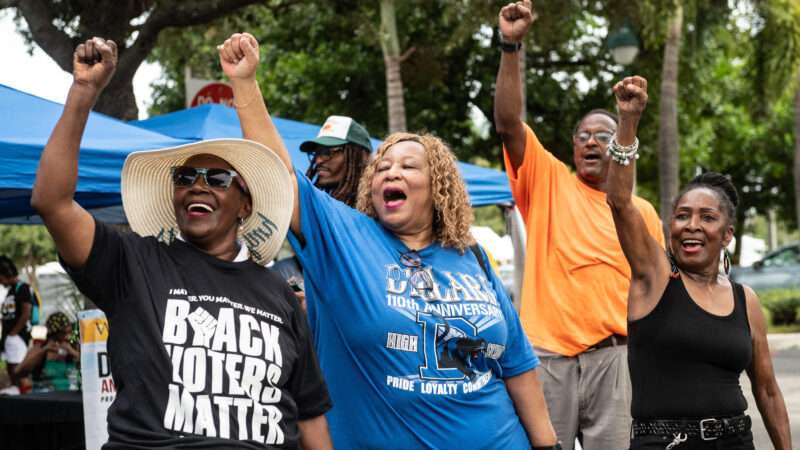 Black voters cheer at an NAACP voting rights rally. One woman is wearing a shirt that says "BLACK VOTERS MATTER"