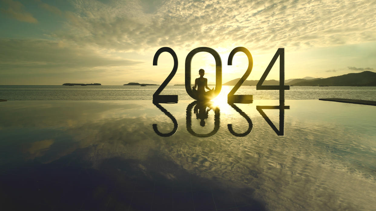 Silhouette of young woman exercising yoga while doing meditation with 2024 new year numbers on the beach at sunrise time