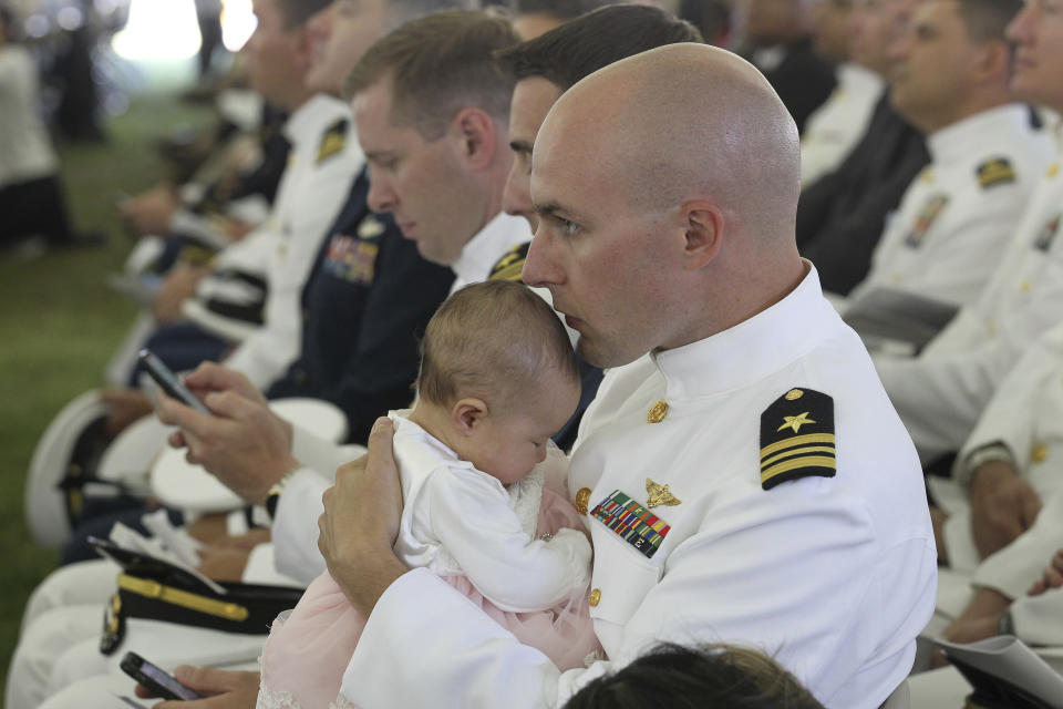 Lt. Cmdr. Darin Wilcken, U.S. Navy, kisses his three-month-old daughter Sky on the head, while waiting to receive his diploma during the U.S. Naval War College's commencement ceremony, Friday, June 14, 2019, in Newport, R.I. (AP Photo/Stew Milne)