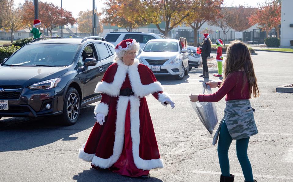 Maggie Munoz, right, 10, hands a bag of arts and crafts to Theresa Bettenhausen, dressed as Mrs. Claus, at the Cookies with Santa at First Baptist Church organized by Mary Campbell, of Macaroni Kid Publisher, and sponsored by Lodi Fire Department in Lodi, California, Saturday, Dec. 5, 2020. Santa personally delivers cookies to each car in this drive-up fundraiser for Macaroni Kids. A portion of the proceeds goes to the Lodi Fire Foundation. [SARA NEVIS/FOR THE RECORD]