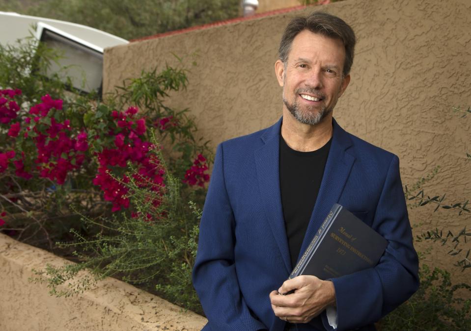 Geodesist Michael Dennis, NOAA's National Geodetic Survey, holds a copy of the Manual of Surveying Instructions Thursday, Nov. 21, 2019, in Laveen, Ariz. The small difference between the U.S. survey foot and the international foot caused trouble in planning for high speed rail in California, and created a mess for bridge work between Oregon, which uses the international foot, and Washington, which uses the U.S. one, he says. (AP Photo/Ross D. Franklin)