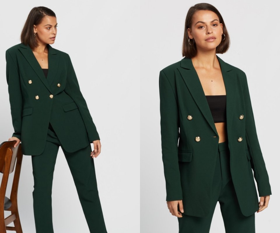 A dark haired girl wears a dark green blazer with gold buttons against a white backdrop.