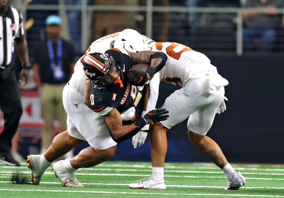 Oklahoma State's Ollie Gordon II (0) is tackled by Texas's Byron Murphy II (90) and Jerrin Thompson (28) in the first half of the Big 12 Football Championship game between the Oklahoma State University Cowboys and the Texas Longhorns at the AT&T Stadium in Arlington, Texas, Saturday, Dec. 2, 2023.