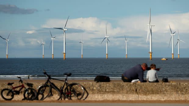 A man and child sitting with bicycles at a coastline near an offshore wind farm.