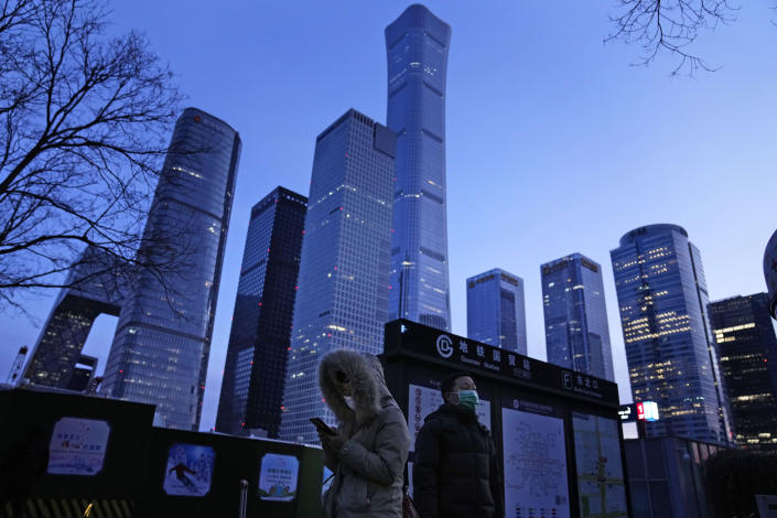 A resident looks at her phone near skyscrapers at the central business district in Beijing, China, Wednesday, Jan. 26, 2022. Richer, more heavily armed and openly confrontational, China has undergone history-making change since the last time it was an Olympic host in 2008. (AP Photo/Ng Han Guan)